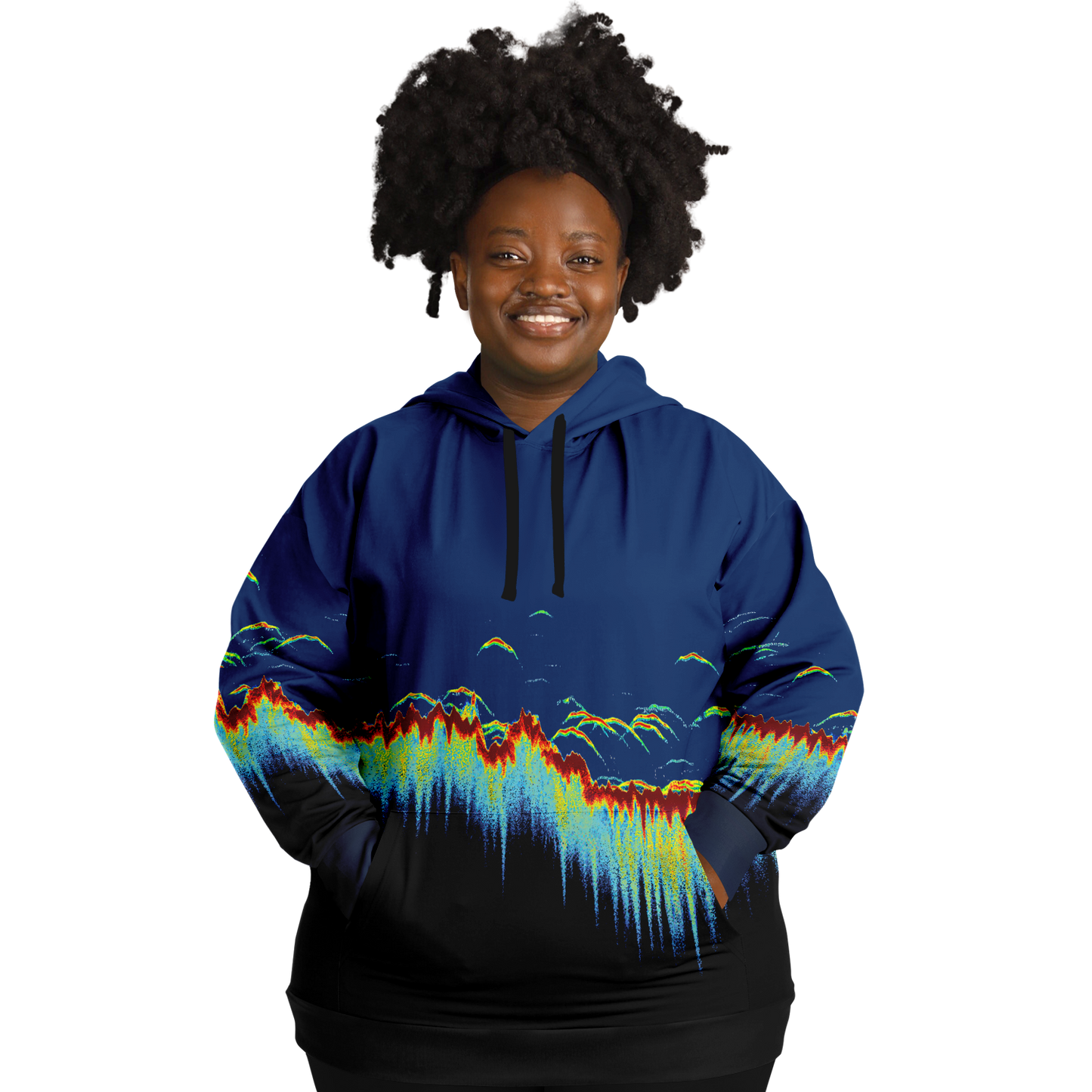 A person wearing a Sonar Scan Plus-size Hoodie, featuring vibrant abstract wave patterns, stands smiling against a black background. Their curly hair complements the playful design, exuding a cheerful demeanor that makes this piece an ideal addition to any fishing wardrobe.