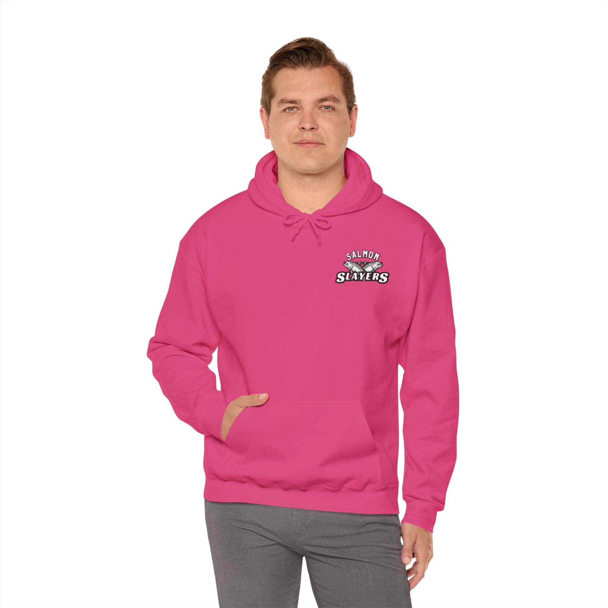 A person wearing a vibrant pink Salmon Slayers - Twin Salmon Logo Hoodie, with "Salmon Slayers" printed on it, stands against a plain white background. This unisex hoodie, crafted from a cotton/poly blend featuring ethically grown cotton, includes a front pocket. The person pairs it with gray pants.