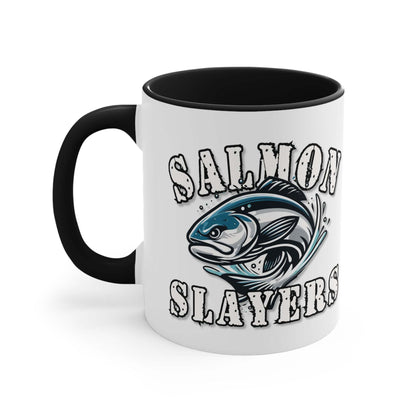 A white custom Salmon Slayers - Fierce Flash - Accent Coffee Mug, 11oz with a blue interior and C-handle features the design "Salmon Slayers" with a stylized illustration of a salmon in the center. The mug, showcasing an eye-catching color contrast, is placed on a wooden surface next to a small macaron, coffee beans, and a spoon.