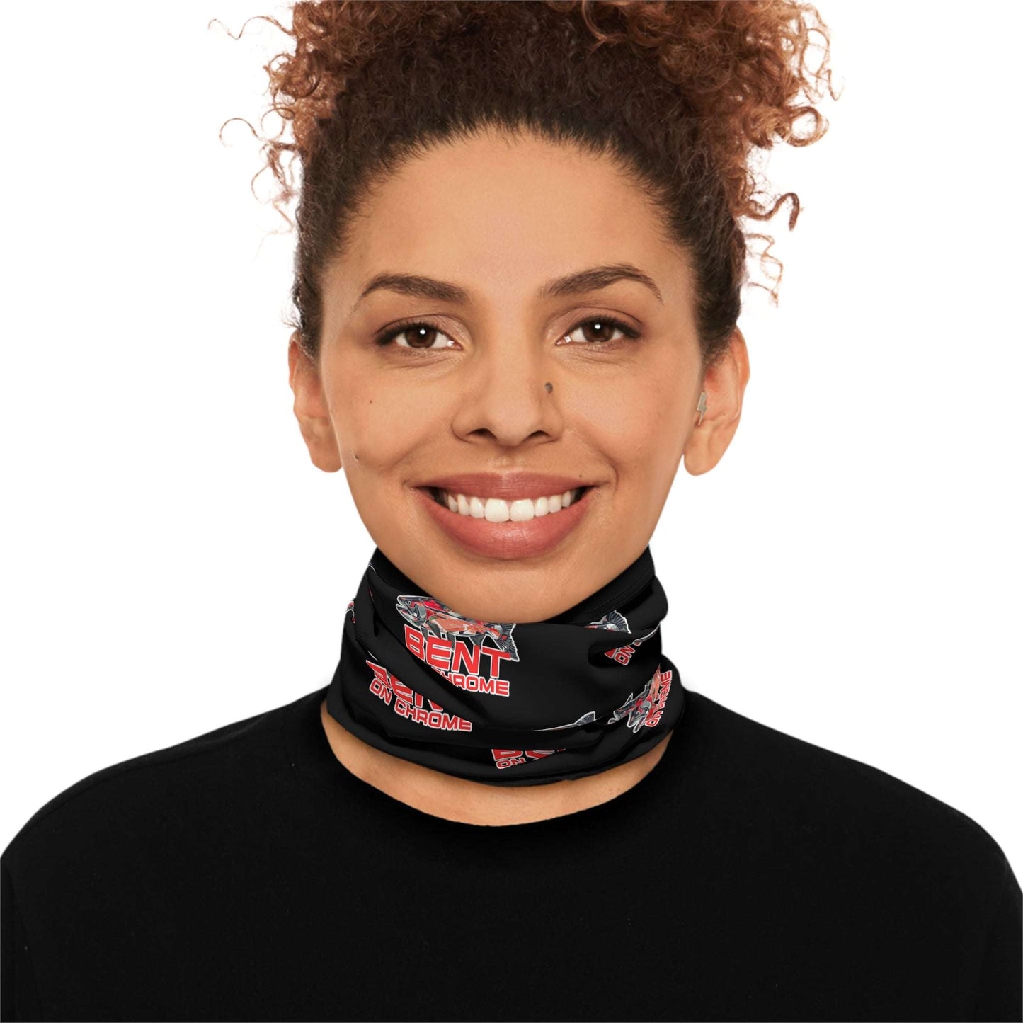 A woman with curly hair wears a Bent On Chrome - Lightweight Neck Gaiter - Red Salmon Logo Black with red and white graphics, including text and a stylized image of a snowmobile. She looks directly at the viewer, dressed in a.