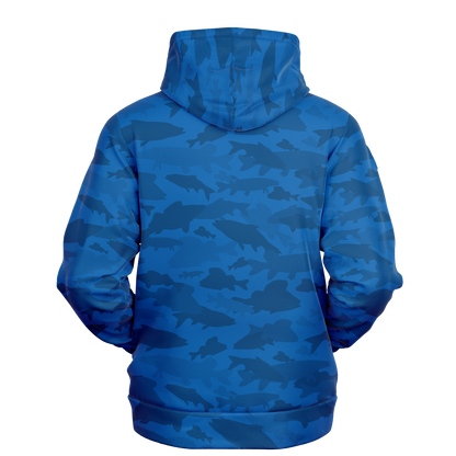 A person wearing an Angler's Mirage Pull Over Hoodie in a fish camo pattern stands against a black background. The design, showcasing various shades of blue, creates a textured and dynamic appearance. With the hood up, the handcrafted hoodie covers their head.