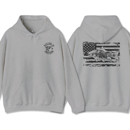 The Reeling In Freedom - Cotton/Poly Blend - Hoodie, ideal for any fishing enthusiast, is depicted from the front and back. The front showcases a small fish graphic accompanied by "Feeling of Freedom" text on the left chest, while the back prominently features a large fish graphic set against a distressed American flag design, celebrating American pride.