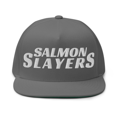 The Salmon Slayers - Flat Bill Cap is a stylish gray baseball hat made from cotton twill, set against a black background and boldly embroidered with "SALMON SLAYERS" in white. It features a snapback closure to ensure the perfect fit.