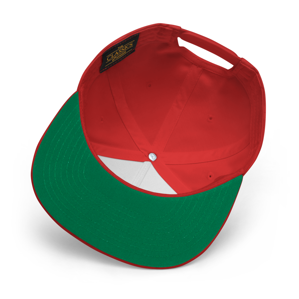 The image showcases the underside of the Salmon Slayers - Flat Bill Cap, which features a red crown with a green brim and snapback closure. Made from cotton twill, the interior is adorned with a black label featuring gold text, white lining under the crown, and a central metal button. The cap is artfully displayed against a black background.