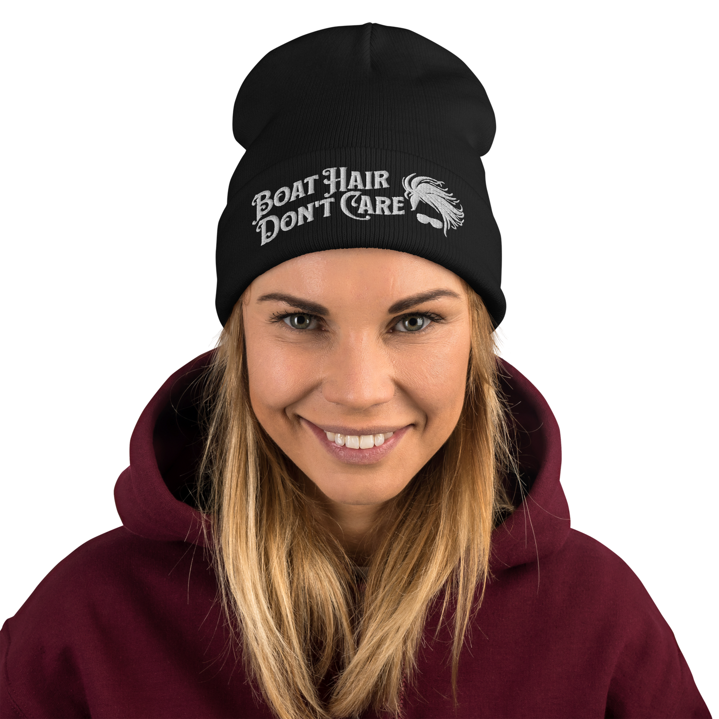 A cozy, dark green beanie with a folded brim showcases the embroidered white text "BEANIE - BOAT HAIR DON'T CARE" alongside a whimsical design of windblown hair and sunglasses.