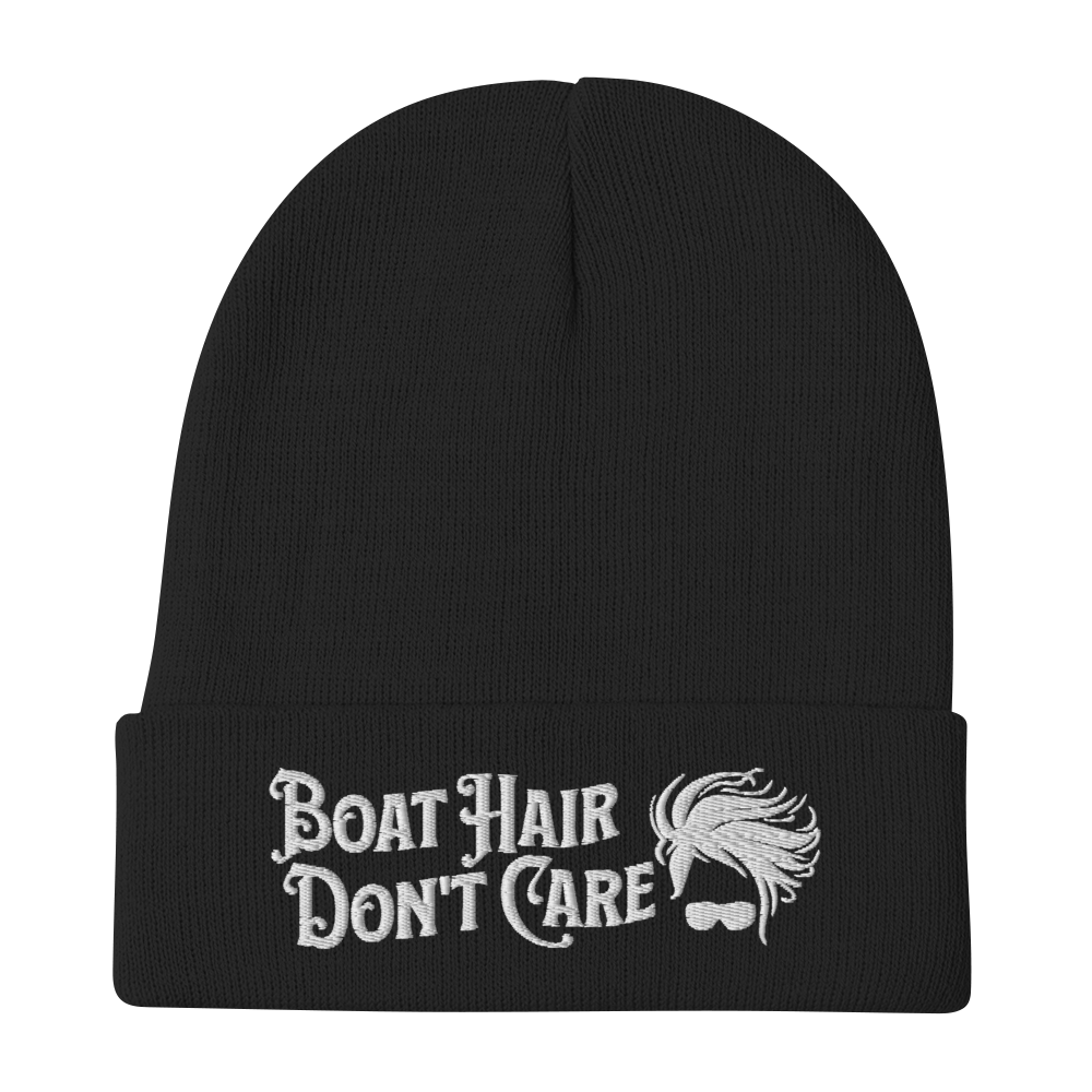 A cozy, dark green beanie with a folded brim showcases the embroidered white text "BEANIE - BOAT HAIR DON'T CARE" alongside a whimsical design of windblown hair and sunglasses.