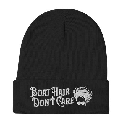 A cozy, dark green beanie with a folded brim showcases the embroidered white text "BEANIE - BOAT HAIR DON'T CARE" alongside a whimsical design of windblown hair and sunglasses.