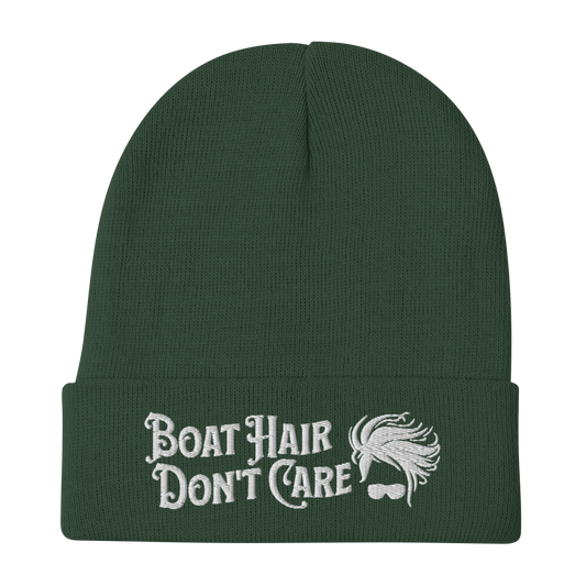 A cozy, dark green beanie with a folded brim showcases the embroidered white text "BEANIE - BOAT HAIR DON'T CARE" alongside a whimsical design of windblown hair and sunglasses.