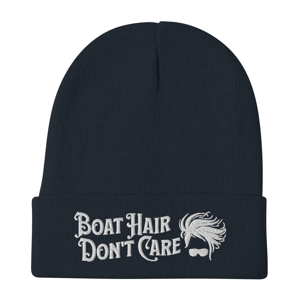 A cozy, dark green beanie with a folded brim showcases the embroidered white text "BEANIE - BOAT HAIR DON'T CARE" alongside a whimsical design of windblown hair and sunglasses.