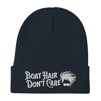 A cozy, dark green beanie with a folded brim showcases the embroidered white text "BEANIE - BOAT HAIR DON'T CARE" alongside a whimsical design of windblown hair and sunglasses.