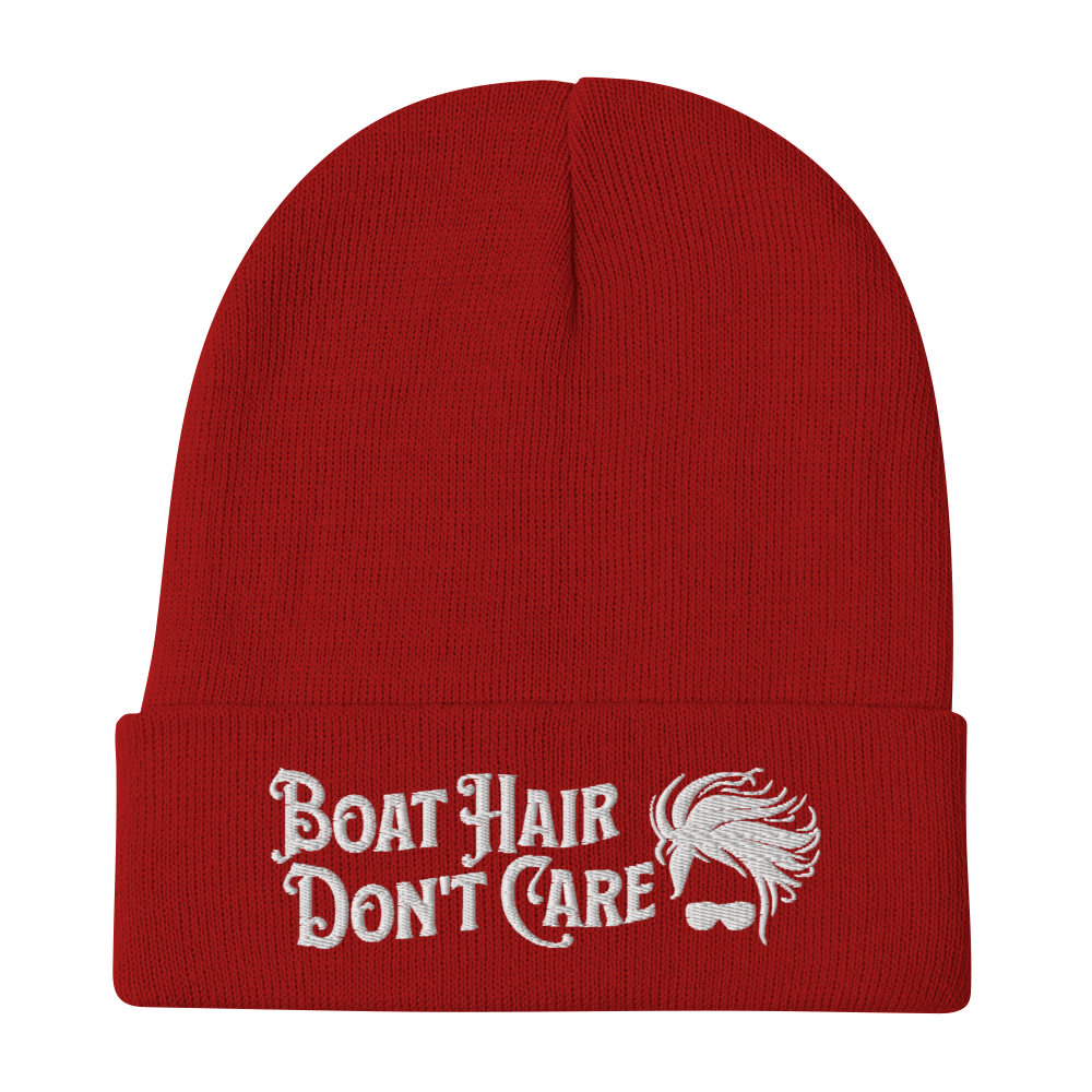 A cozy, dark green beanie with a folded brim showcases the embroidered white text "BEANIE - BOAT HAIR DON'T CARE" alongside a whimsical design of windblown hair and sunglasses.