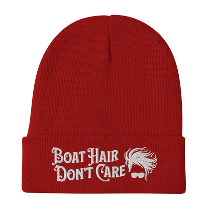 A cozy, dark green beanie with a folded brim showcases the embroidered white text "BEANIE - BOAT HAIR DON'T CARE" alongside a whimsical design of windblown hair and sunglasses.