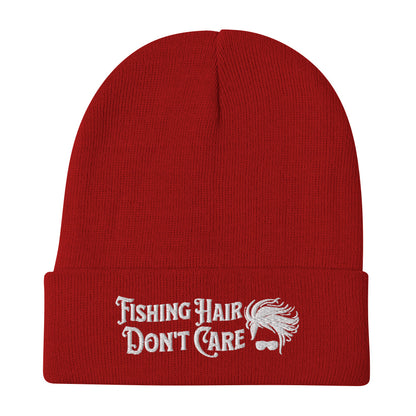 The "Fishing Hair Don't Care - Embroidered Beanie" is a red fishing beanie featuring white embroidery that reads "Fishing Hair Don't Care," along with a small illustration of a messy hairstyle above sunglasses, making it perfect for fishing enthusiasts.