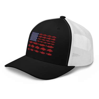 This Fishy Flag Trucker Cap is a black baseball cap featuring an American flag design made up of fish. The blue and white stars section is in the top left, while the red stripes are composed of small fish silhouettes, making it perfect for fishing enthusiasts.