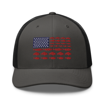 This Fishy Flag Trucker Cap is a black baseball cap featuring an American flag design made up of fish. The blue and white stars section is in the top left, while the red stripes are composed of small fish silhouettes, making it perfect for fishing enthusiasts.