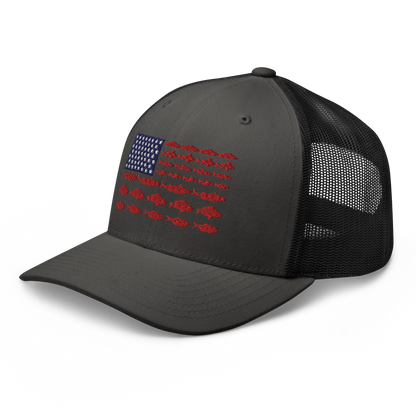 This Fishy Flag Trucker Cap is a black baseball cap featuring an American flag design made up of fish. The blue and white stars section is in the top left, while the red stripes are composed of small fish silhouettes, making it perfect for fishing enthusiasts.