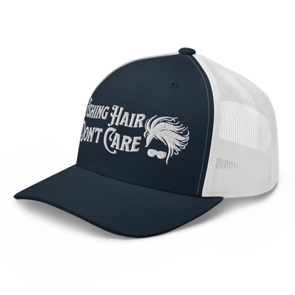 A black and white Fishing Hair, Don't Care - Trucker Style Fishing Cap with a curved brim and mesh back. The front of the cap features the embroidered text "Fishing Hair Don't Care" in white thread next to an image of stylized windblown hair and stylish sunglasses, perfect for fishing enthusiasts.