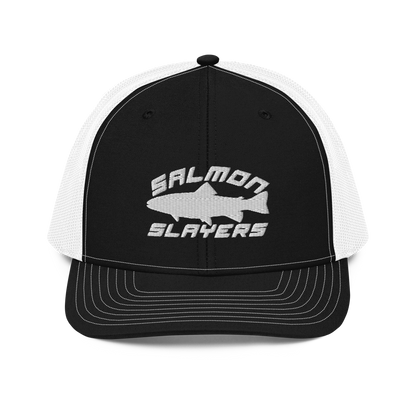 A Salmon Slayers - Sport - Richardson 112 - Trucker Cap with the text "SALMON SLAYERS" embroidered in white on the front. Above the text, there is an outline of a salmon fish. The cap features stitching details on the brim and offers a structured fit. The background is solid black.